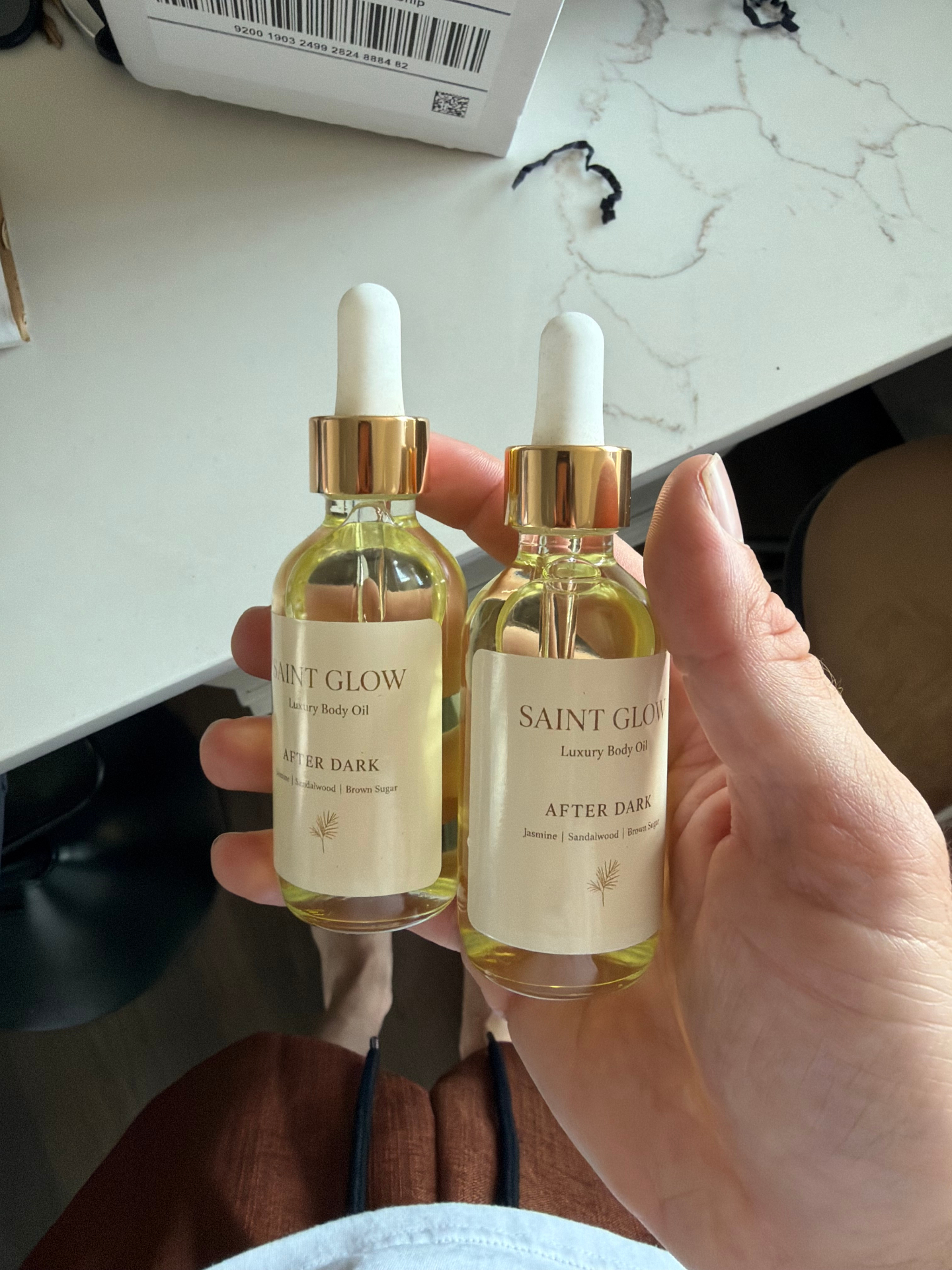 Customer holding two bottles of Saint Glow After Dark body oil in warm light